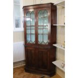A late Georgian mahogany standing corner cabinet, having a pair of glazed doors enclosing three