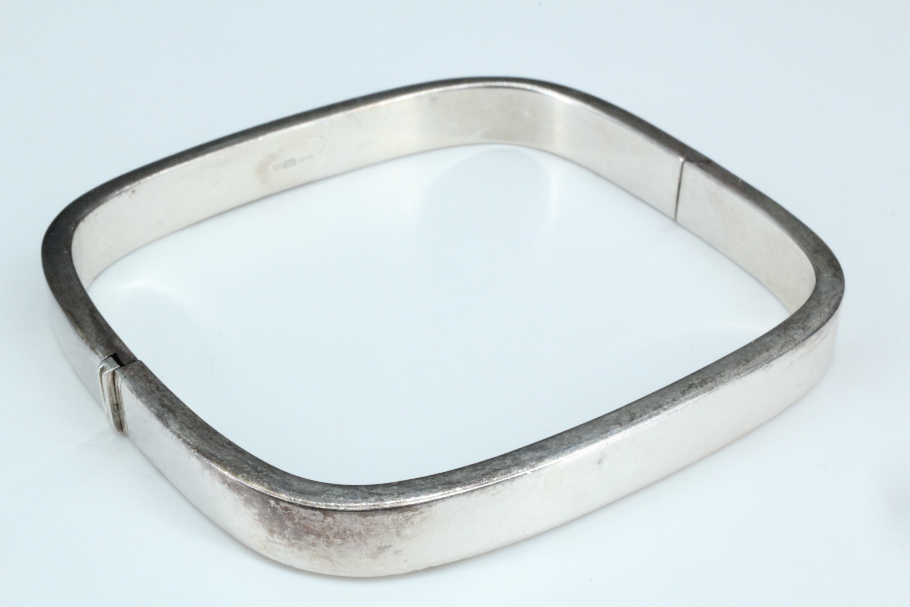 A contemporary silver bangle, of rectangular section and square form, having a flush knuckle hinge