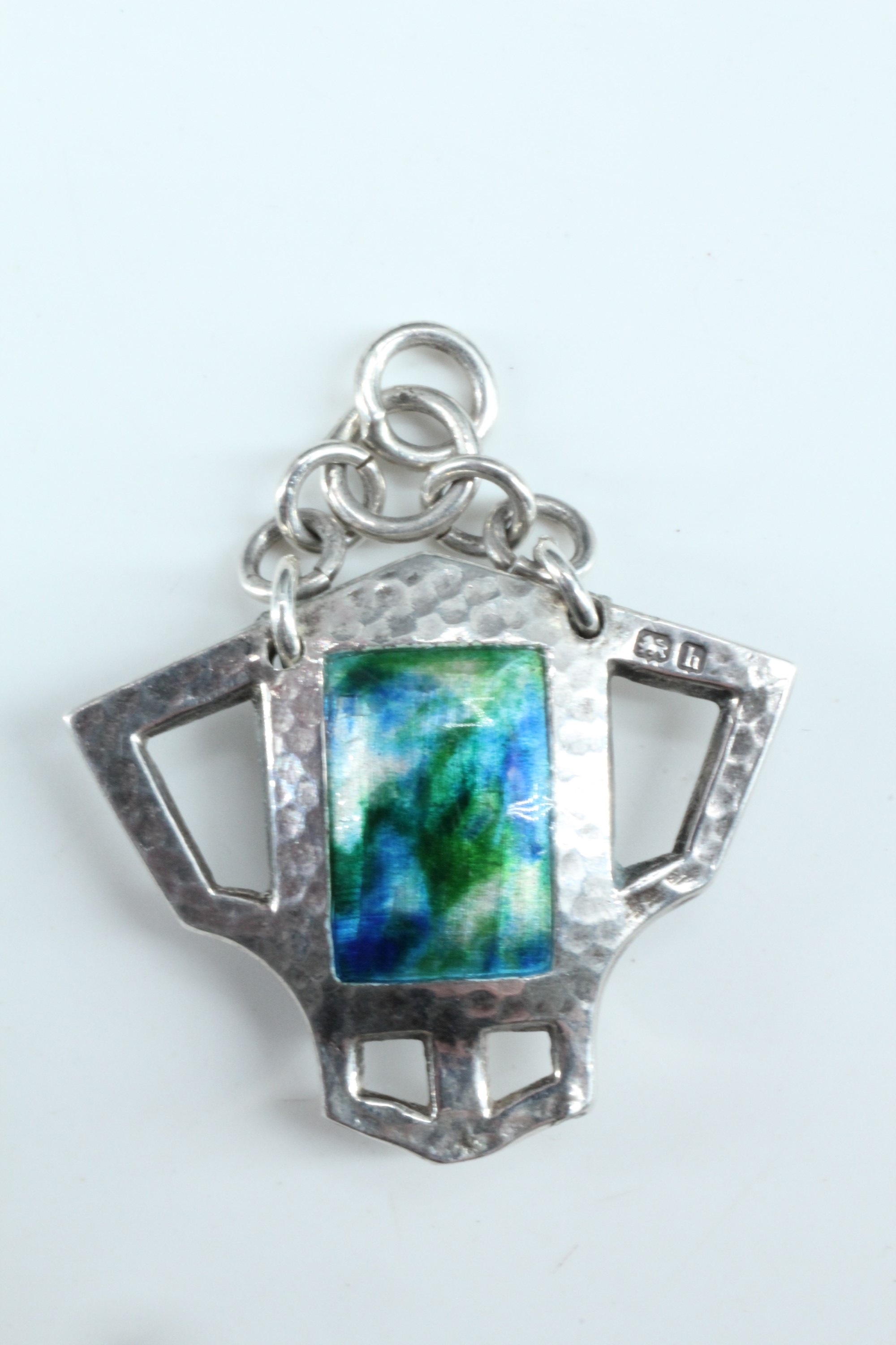 An Edwardian Arts and Crafts enamelled silver pendant, of geometric form, planished and centred by