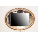 An oval wall mirror, having a bevel-edged plate in antiqued gilt frame, 67 cm x 52 cm
