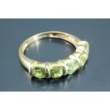 A five stone dress ring, having five 4 mm round green stones, line set between gold batons on