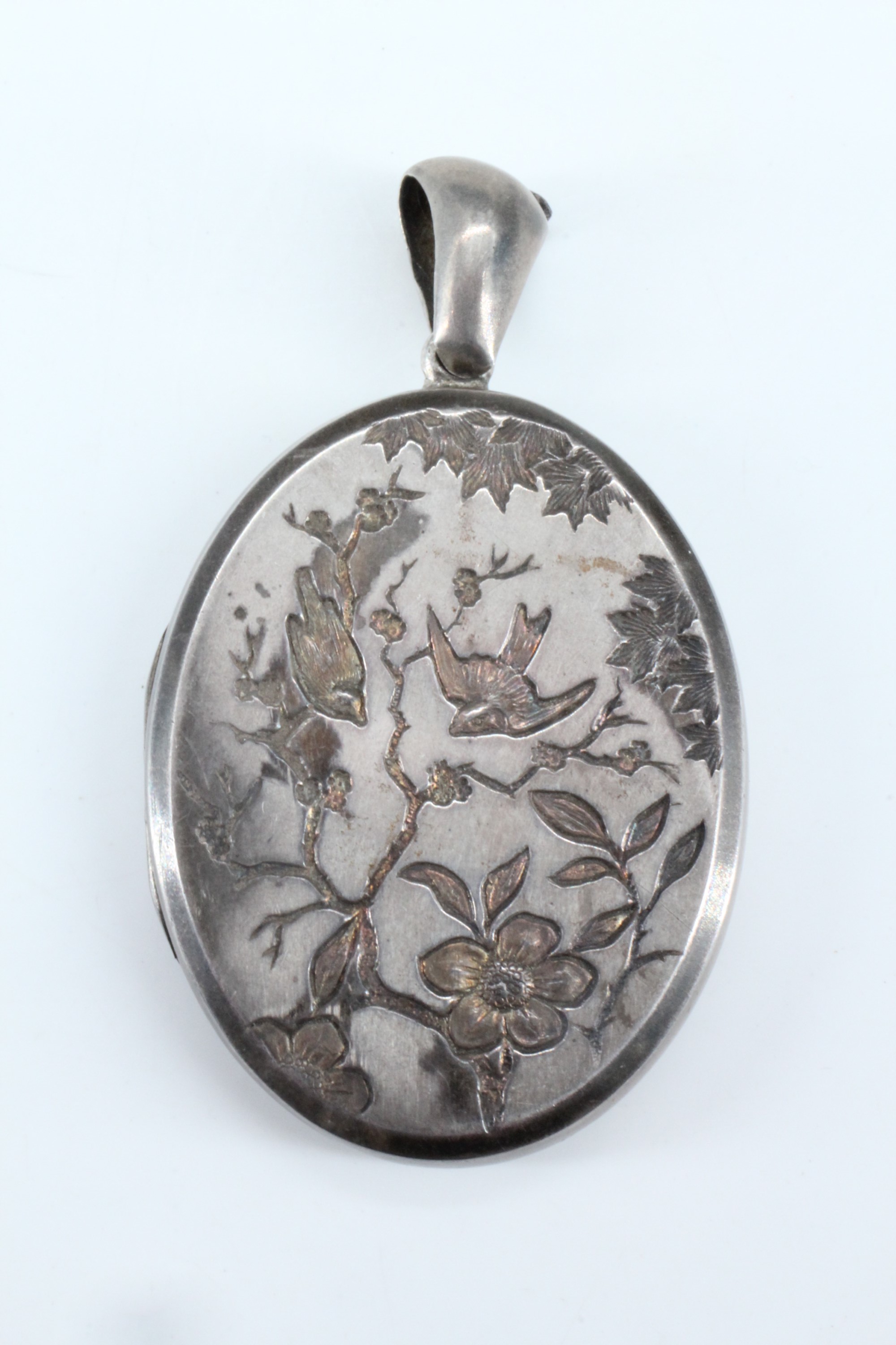 A Victorian Aesthetic Movement influenced white metal double pendant locket, its face shallow relief