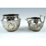 An early 20th Century silver cream jug and sugar bowl, of squat form with repousse scrolls and
