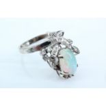 An asymmetric opal and diamond dress ring, the shoulders morphing into diamond set crossing ribbons,