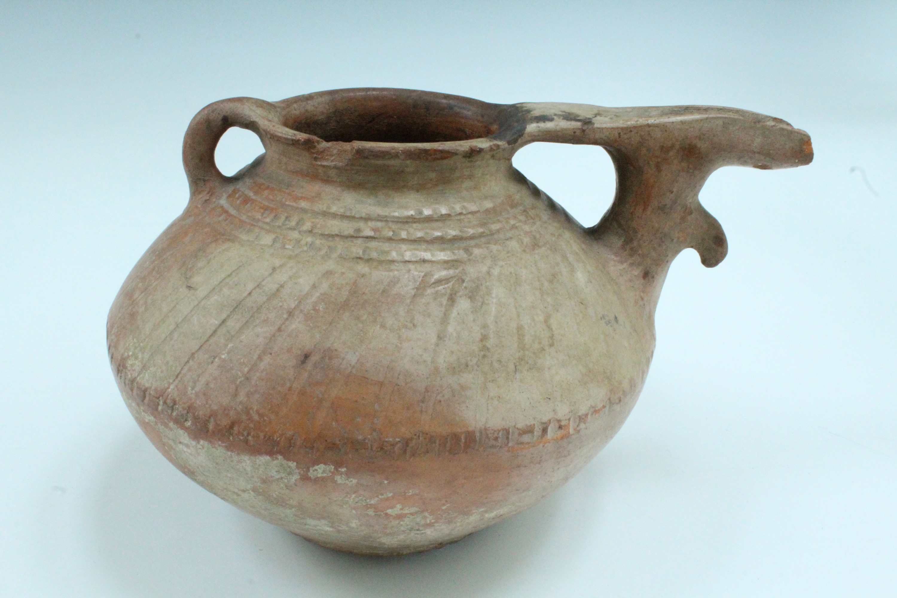 An ancient Luristan earthenware spouted vessel, of lenticular form with bridged spout and opposed