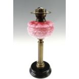 A late 19th Century columnar oil lamp, having a pink glass reservoir, on a tiered black-glazed base,
