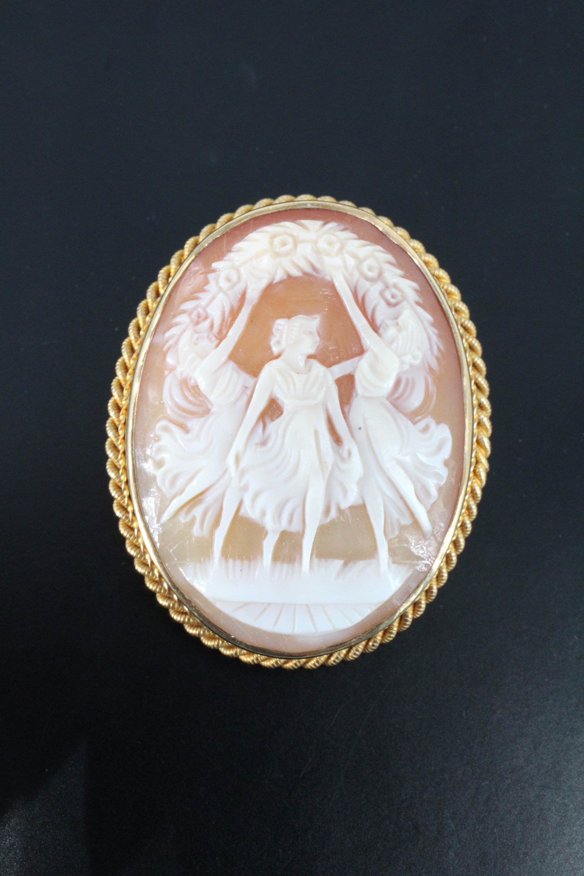 A 9 ct gold shell cameo brooch, depicting three girls dancing beneath a garland, bezel set and