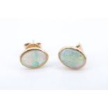 A modern pair of opal ear studs, having 7 x 6 mm oval opals bezel set on a yellow metal (tests as