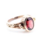 A 21st Century lady's almandine ring, having an oval garnet (9 x 6 mm) in a rubbed setting between