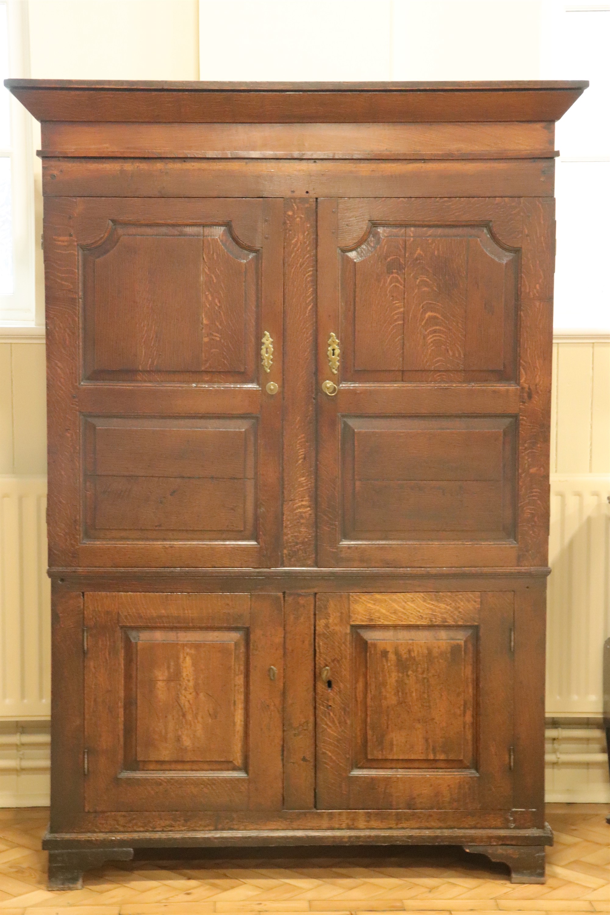 An early 19th Century joined oak press cupboard, having an angular cornice above a pair of fielded-