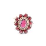 A garnet flowerhead cluster ring, comprising a central oval facet-cut stone of approx 6 mm x 4 mm