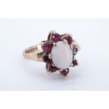 An opal and ruby dress ring, comprising an oval opal cabochon of approx 8 mm x 6 mm framed by