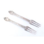 A pair of 17th Century white metal trefid sweetmeat forks, each foliate scroll engraved, their
