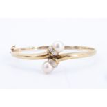 A 9 ct gold, pearl, and diamond hinged bangle, of faux torque form, its terminals set with 8 mm