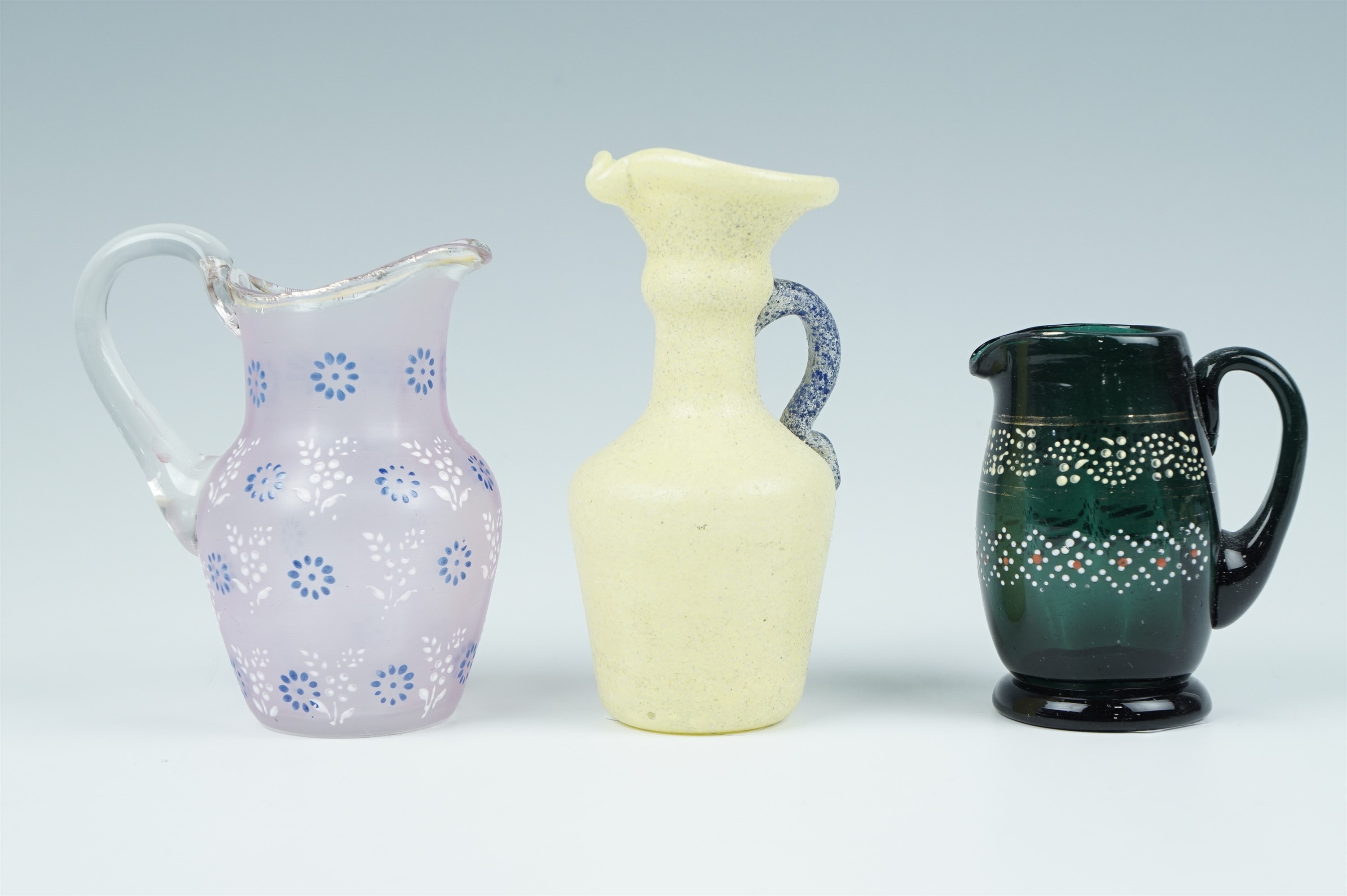 Three Victorian small glass jugs, two having jeweled enamel decoration and one having a speckled