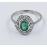 Platinum ring set with oval central emerald surrounded by a pierced band set with diamonds A