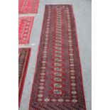 Pakistan runner of Turkoman design with a single row of gols on a wine ground with borders, 8ft x