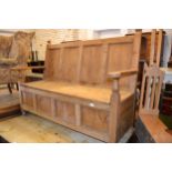 Stripped pine settle with a four panelled back and a box seat, a panelled front and low turned