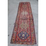 Kurdish runner with a repeating medallion design on brick red field with borders, 10ft 10ins x 3ft