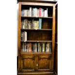 20th Century oak bookcase, the moulded cornice above open shelves and two arched panelled doors on a