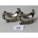 Pair of Continental silver figural mounted boat shaped salts cast with floral relief decoration