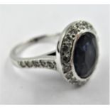 18ct White gold ring, the central oval sapphire surrounded by diamonds, the shoulders inset with