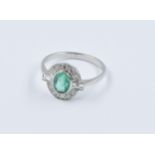 Platinum ring set with a central oval emerald surrounded by diamonds, size N