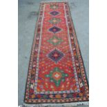Karaja runner with seven hooked medallions on a brick red ground with borders, 9ft 10ins x 2ft 10ins