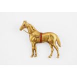 A GOLD AND ENAMEL STANDING RACEHORSE BROOCH realistically formed, with ruby eye, 3.3cm high, circa