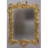 A GILTWOOD WALL MIRROR, of shaped rectangular form, the frame with scrolling and pierced flower