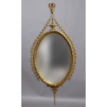 A GILT WALL MIRROR, the bevelled oval plate set within a gesso frame with ribbon and urn pediment