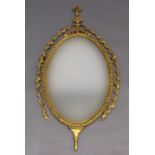 A GILT WALL MIRROR, the bevelled oval plate beneath a ram's head urn pediment and trailing