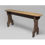 AN ARTS AND CRAFTS OAK BENCH OR OCCASIONAL TABLE, the rounded rectangular top on carved trestle