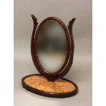 A 19TH CENTURY MAHOGANY PLATFORM MIRROR, the oval plate supported on a leaf carved frame