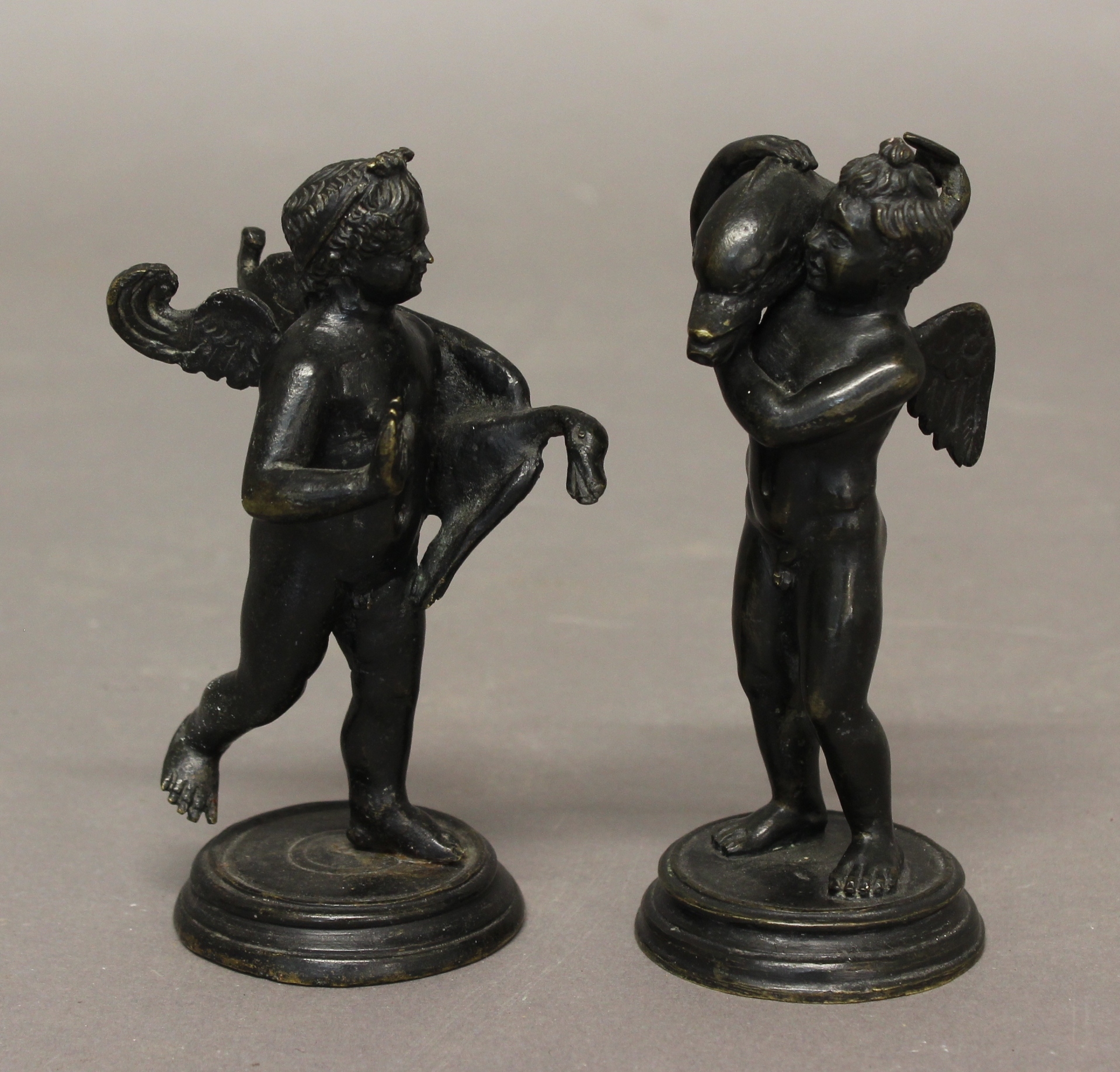 A PAIR OF ITALIAN BRONZE PUTTI, taming a swan and a dolphin, on circular bases, height of tallest