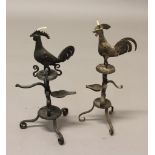 A PAIR OF FOLK ART WROUGHT IRON OIL LAMPS, in the form of cockerels on scrolling tripod bases,