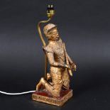 SOUTH EAST ASIAN GILT METAL FIGURAL LAMP. A gilt metal figure with elaborate clothing, crouched on