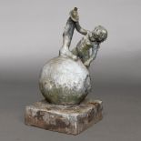 A LEAD CHERUB SEATED ON A BALL.