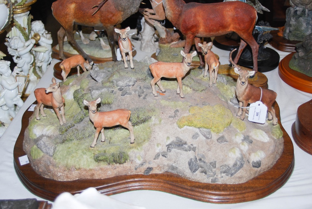 A LARGE SCOTTISH ART PAINTED RESIN FIGURE OF A HERD OF RED DEER ON A ROCKY OUTCROP ON A WOODEN BASE,