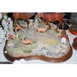 A LARGE SCOTTISH ART PAINTED RESIN FIGURE OF A HERD OF RED DEER ON A ROCKY OUTCROP ON A WOODEN BASE,