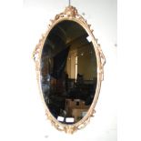 GILT METAL OVAL WALL MIRROR WITH FOLIATE SURMOUNT AND SCROLL DETAIL.