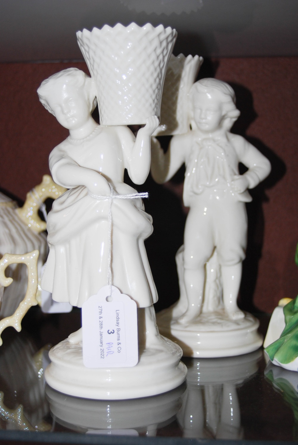 PAIR OF BELLEEK PORCELAIN FIGURAL SPILL VASES, MOULDED WITH BOY AND GILR HOLDING ALOFT BASKETS, BLUE