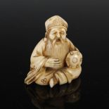 A Japanese carved ivory netsuke, probably Meiji Period, depicting a seated man playing a drum,