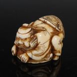 A Japanese carved ivory netsuke, possibly Edo period, depicting Ashoki covering an Oni with a