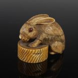 A Japanese carved ivory netsuke / okimono, probably Meiji Period, depicting a rabbit on a bowl,