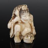 A Japanese carved ivory netsuke, possibly Edo period, depicting a seated man in a cape of leaves