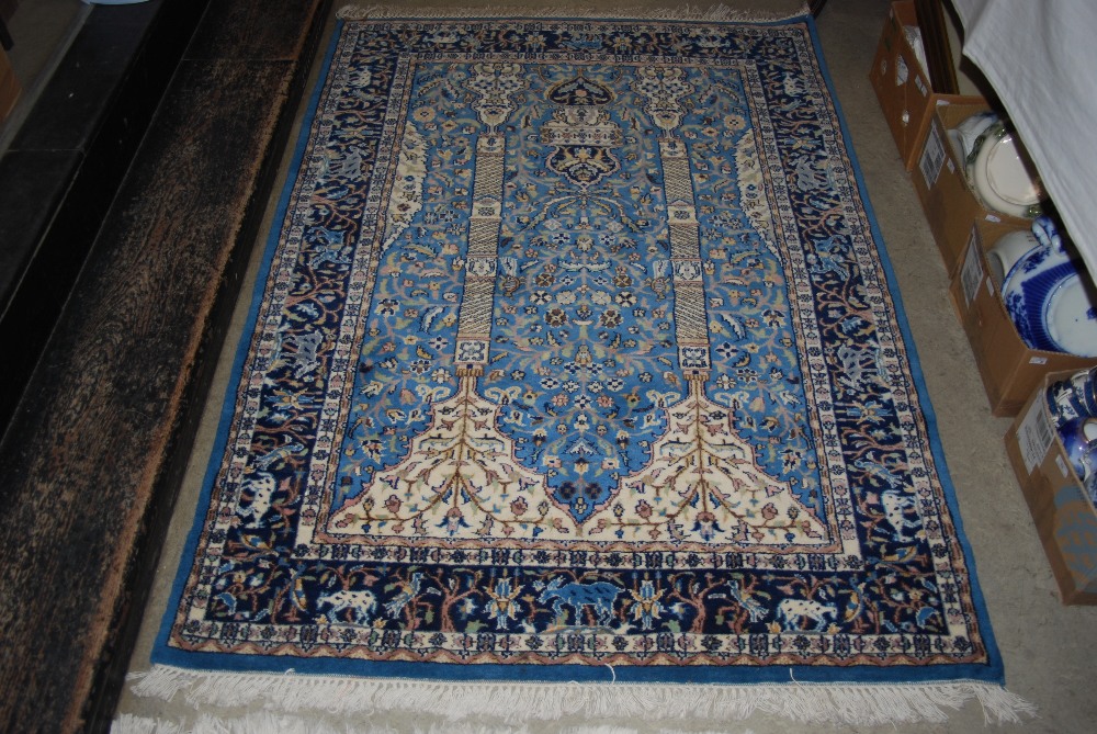 A MACHINE MADE BLUE GROUND PERSIAN STYLE RUG WITH CENTRAL MIRHAB PANEL ENCLOSING TREE OF LIFE WITHIN