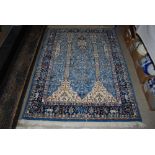 A MACHINE MADE BLUE GROUND PERSIAN STYLE RUG WITH CENTRAL MIRHAB PANEL ENCLOSING TREE OF LIFE WITHIN