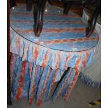 CIRCULAR DRAPE TABLE WITH ORANGE AND BLUE COLOURED FABRIC.