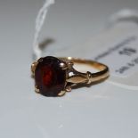 A 9CT GOLD DRESS RING SET WITH FACET CUT GLASS RED COLOURED OVAL STONE.
